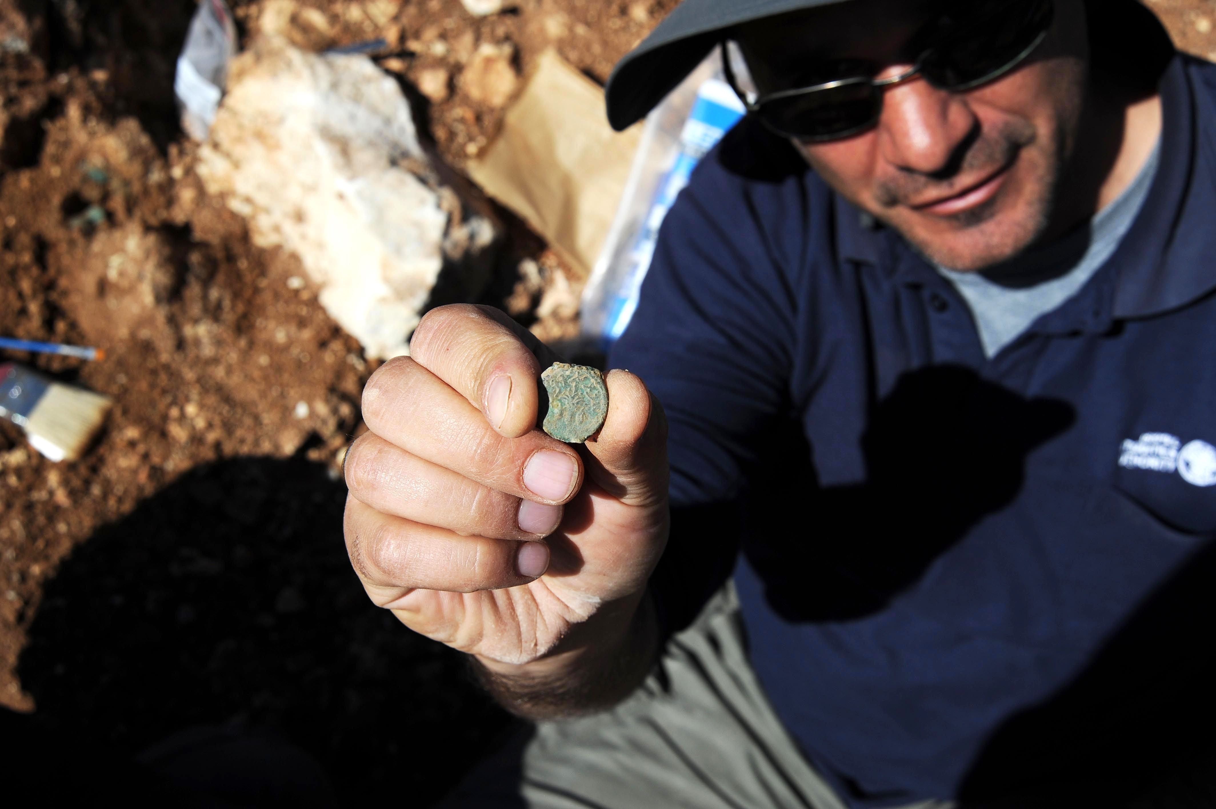 IAA archaeologist Pablo Betzer holds up a Jewish Revolt coin found outside Jerusalem