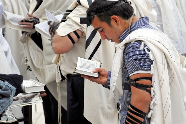 Jewish men wearing tallitot (prayer shawls) pray with tefillin (phylacteries) and siddurim (Jewish prayer books).