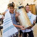 Two 13-year-old Jewish boys share the weight of carrying a Torah scroll encased by a silver Torah tik.