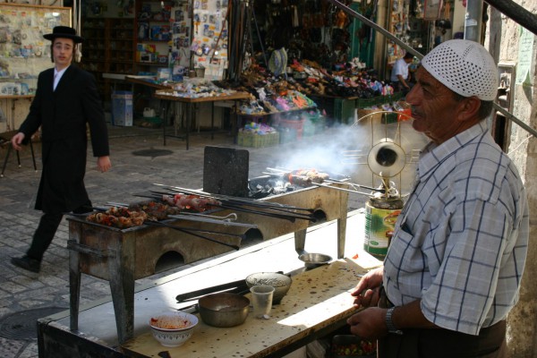 A Hassidic teenager glances toward an Arab grilled-meat stand in Jerusalem.