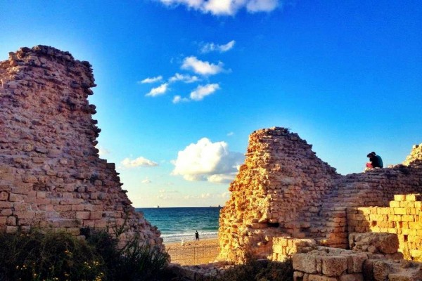 A couple sits together on an ancient wall in Ashdod, Israel, watching the sun go down.