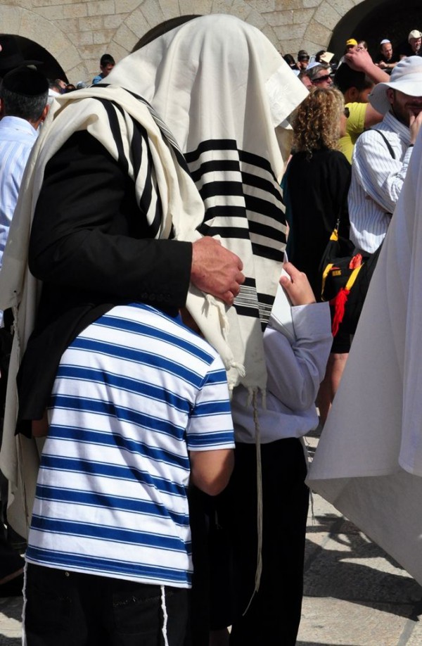 A Jewish father pulls his sons (who are each wearing a tallit katan) under his tallit gadol during the Priestly Blessing at the Western Wall in Jerusalem.