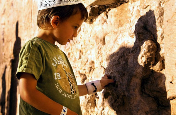 An Israeli child inserts a written prayer into the crevices of the Western (Wailing) Wall, a tradition that arose after the destruction of the Holy Temple, which was situated behind this wall. (Go Israel photo by Noam Chen)