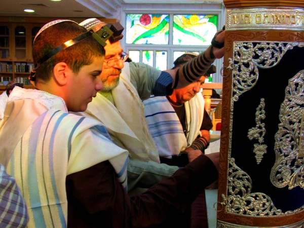 A Jewish 13-year-old male reads from a Torah scroll protected by an elaborately decorated Torah tik.