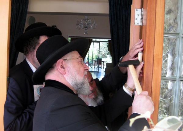 Tel Aviv-Jaffa Chief Rabbi Lau affixes a mezuzah (doorpost) to the front door of the British Ambassador to Israel's Ramat Gan residence in fulfillment of the Biblical injunction to inscribe the words of the Shema "on the doorposts of your house (Deuteronomy 6:9)." The parchment, which is protected in a decorative case, is inscribed with Deuteronomy 6:4–9 and 11:13–21.