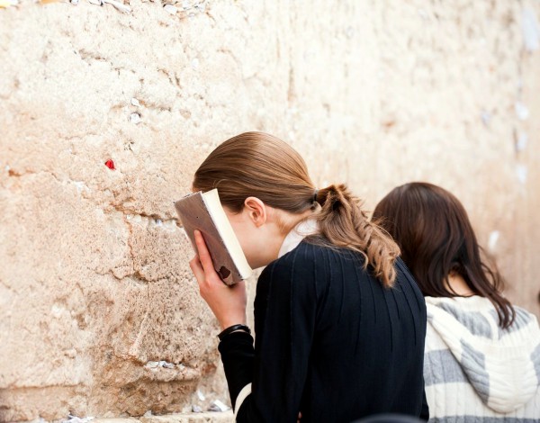 A Jewish young woman buries her face in a siddur (Jewish prayer book) as she prays at the Western (Wailing) Wall.