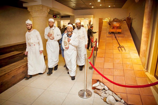 Four Kohanim walk beside a small modular altar in the Temple Institute that can be disassembled and placed within the Third Temple. Two Kohanim carry ceramic vessels filled with pure olive oil that will be stored for use in the Third Temple. On the ramp of the altar is the three-pronged fork for placing the offerings on the fire atop the altar. The copper vessel will be used to remove the previous day's ashes. (Source: Temple Institute Facebook).