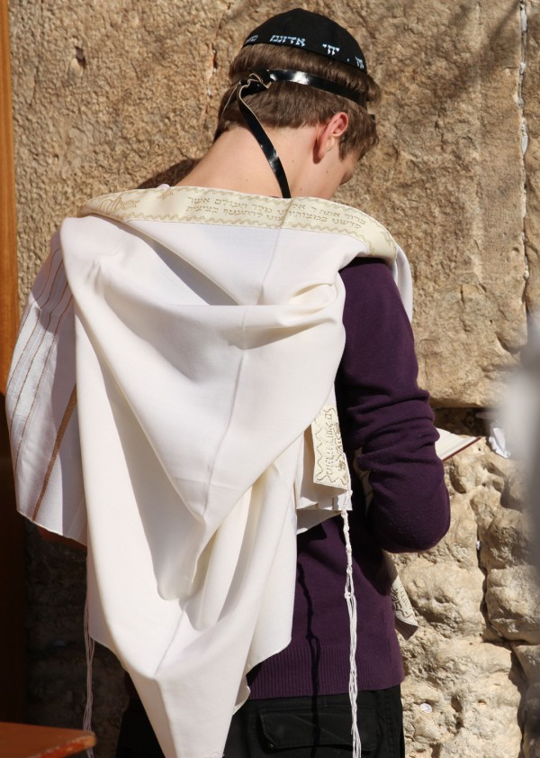 A Jewish teen wearing a tallit (prayer shawl), tefillin (phylacteries), and a kippah (head covering) prays at the Western (Wailing) Wall in Jerusalem. (Photo by the State of Israel)